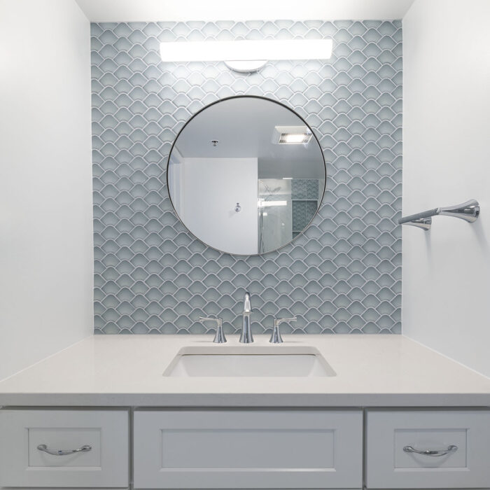 White vanity with round mirror and textured tile